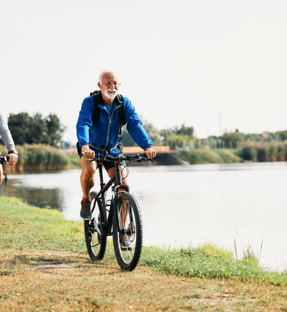 Happy senior athlete and his son riding bicycles by the lake in nature.